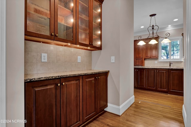 kitchen with decorative backsplash, light hardwood / wood-style flooring, ornamental molding, decorative light fixtures, and light stone counters