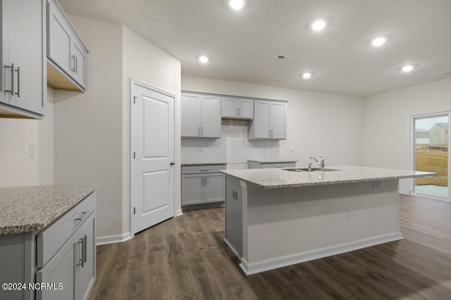 kitchen featuring light stone counters, sink, a center island with sink, gray cabinets, and dark hardwood / wood-style flooring