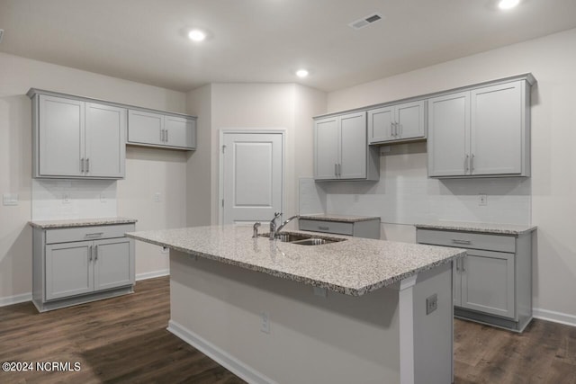 kitchen with sink, a kitchen island with sink, gray cabinets, dark hardwood / wood-style floors, and light stone countertops