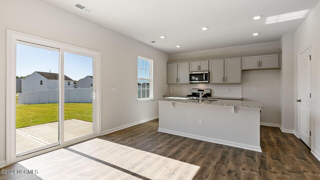 kitchen featuring appliances with stainless steel finishes, gray cabinetry, an island with sink, and a wealth of natural light