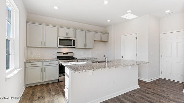 kitchen featuring appliances with stainless steel finishes, a center island with sink, sink, and light stone counters