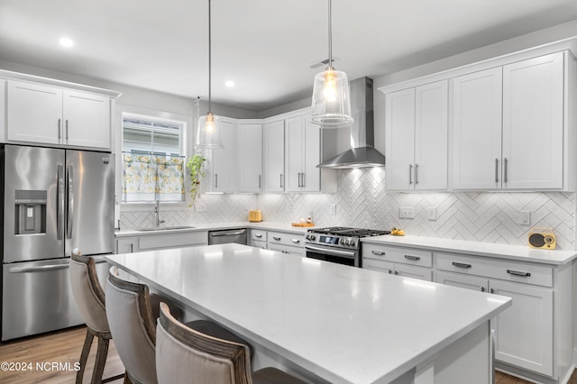 kitchen featuring white cabinetry, wall chimney range hood, decorative light fixtures, and stainless steel appliances