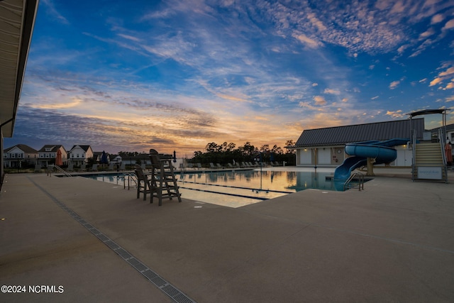 pool at dusk featuring a water slide and a patio