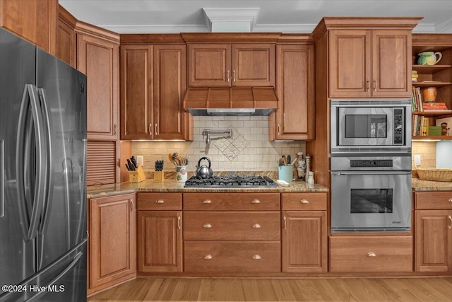 kitchen with light stone counters, appliances with stainless steel finishes, tasteful backsplash, crown molding, and light wood-type flooring