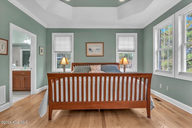 bedroom featuring ensuite bath, a tray ceiling, light hardwood / wood-style flooring, and ornamental molding