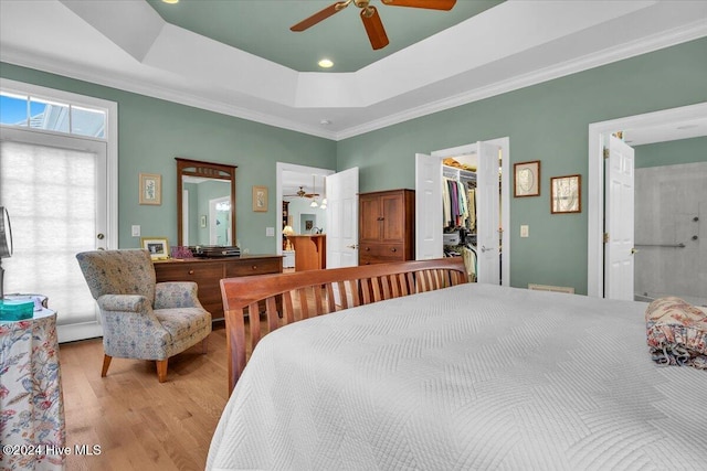 bedroom featuring ensuite bathroom, ceiling fan, a spacious closet, a tray ceiling, and light wood-type flooring