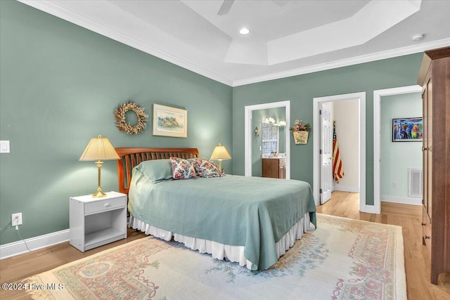 bedroom featuring light hardwood / wood-style floors, ensuite bath, ornamental molding, ceiling fan, and a raised ceiling