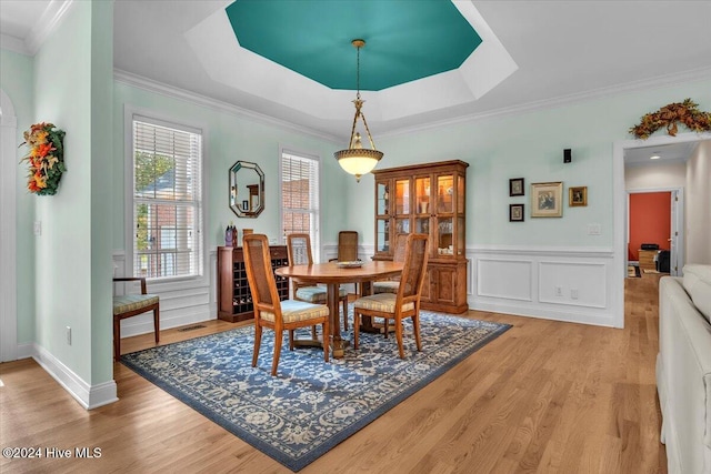 dining space featuring ornamental molding, light wood-type flooring, and a tray ceiling