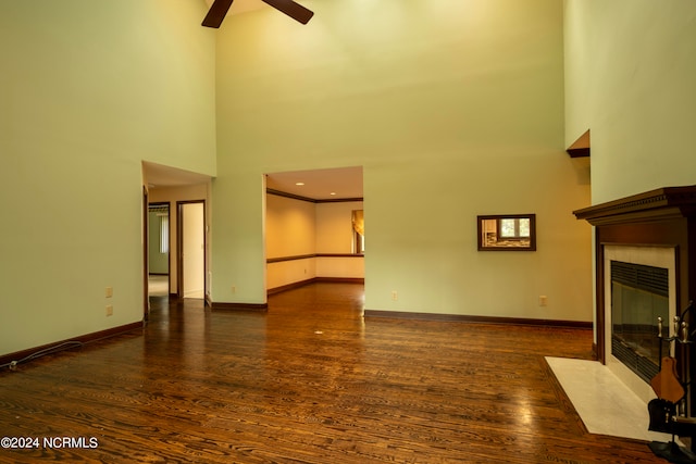 unfurnished living room with ceiling fan, a fireplace, a towering ceiling, and dark hardwood / wood-style floors