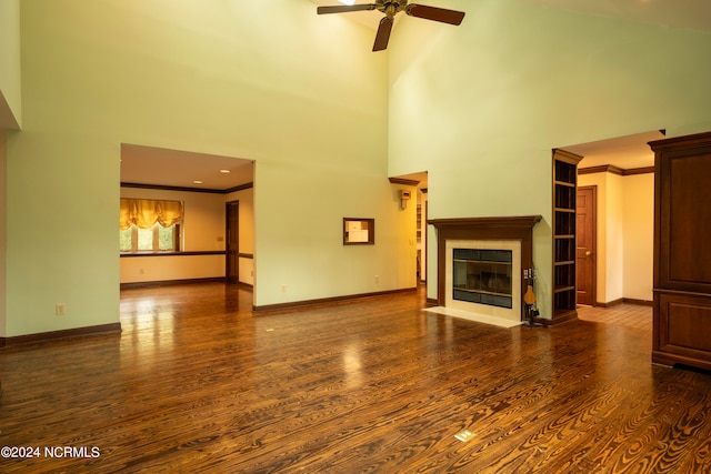 unfurnished living room with a towering ceiling, crown molding, dark wood-type flooring, and ceiling fan