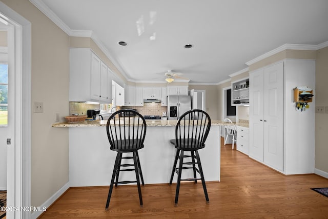 kitchen featuring light hardwood / wood-style floors, tasteful backsplash, kitchen peninsula, stainless steel fridge with ice dispenser, and white cabinetry