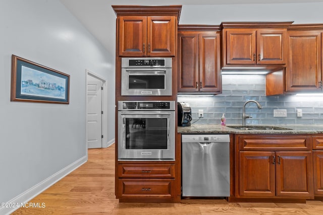 kitchen featuring appliances with stainless steel finishes, decorative backsplash, light stone countertops, light hardwood / wood-style flooring, and sink