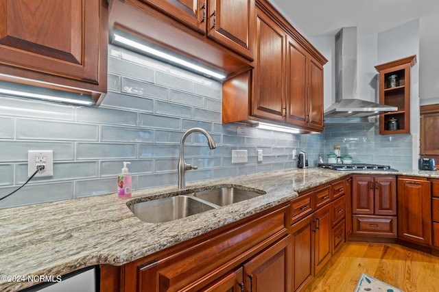 kitchen featuring light wood-type flooring, sink, stainless steel gas stovetop, wall chimney exhaust hood, and light stone countertops