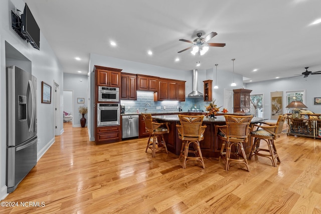 kitchen with light hardwood / wood-style flooring, stainless steel appliances, wall chimney range hood, and a breakfast bar area