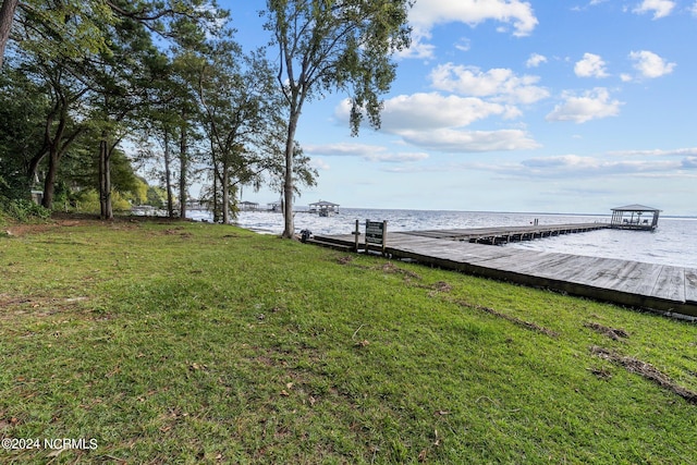 view of dock with a lawn and a water view