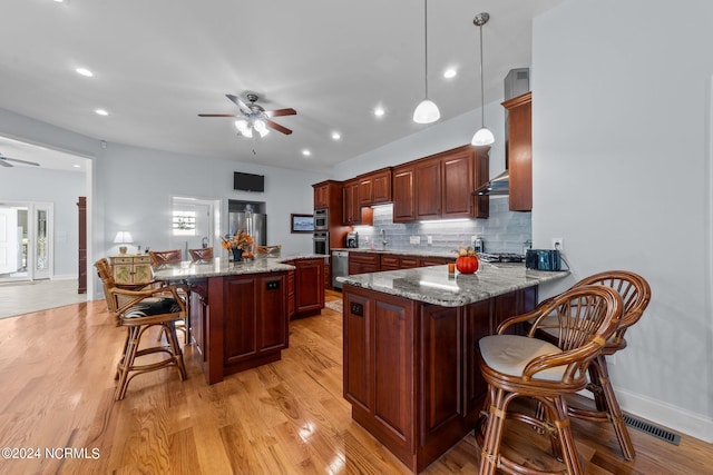 kitchen with appliances with stainless steel finishes, hanging light fixtures, kitchen peninsula, and light hardwood / wood-style flooring