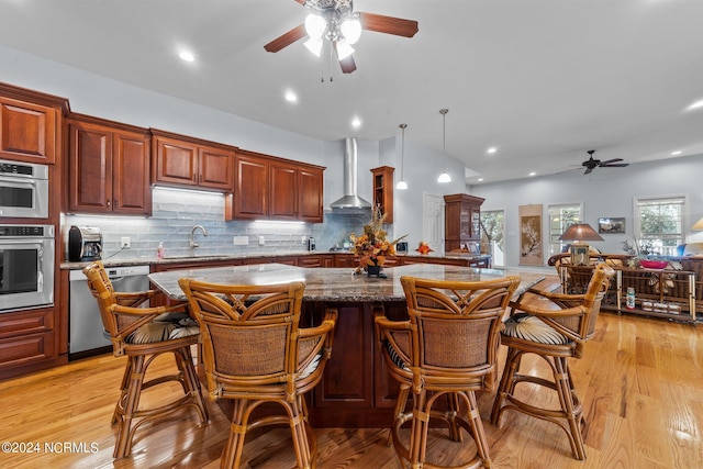 kitchen featuring wall chimney exhaust hood, a sink, backsplash, a ceiling fan, and appliances with stainless steel finishes