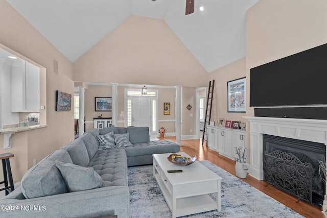 living room featuring ceiling fan, light wood-type flooring, decorative columns, and high vaulted ceiling