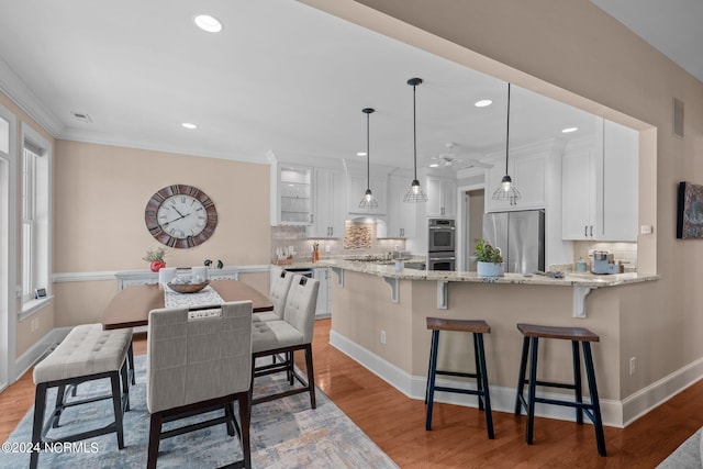 kitchen with pendant lighting, light stone countertops, white cabinetry, appliances with stainless steel finishes, and light wood-type flooring