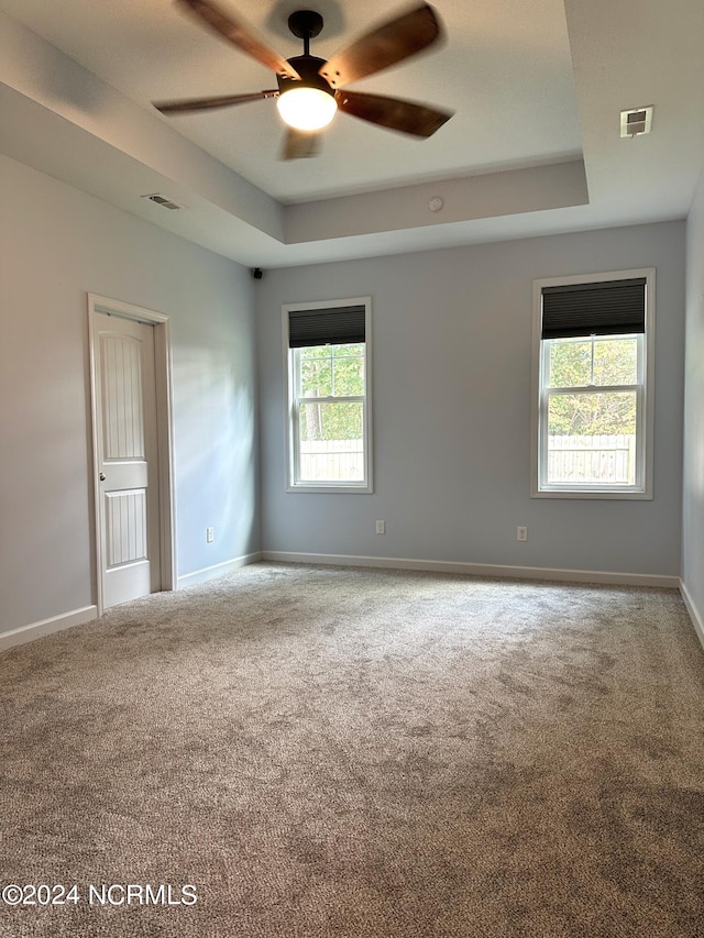 empty room with ceiling fan, a tray ceiling, and carpet flooring