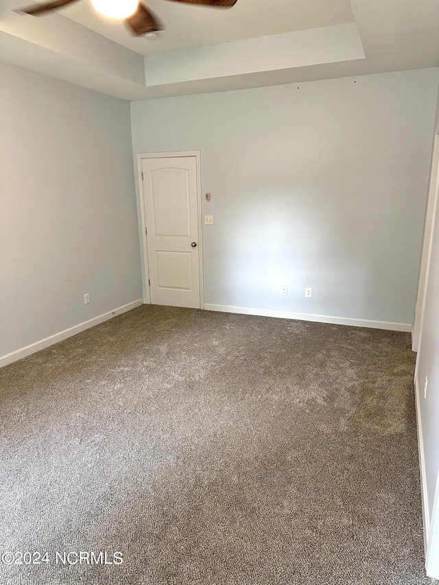 carpeted spare room with a raised ceiling and ceiling fan