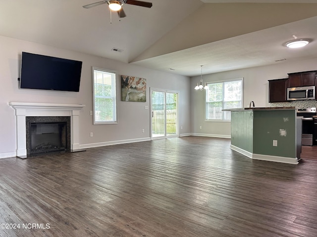 unfurnished living room with ceiling fan with notable chandelier, a wealth of natural light, vaulted ceiling, and dark hardwood / wood-style flooring