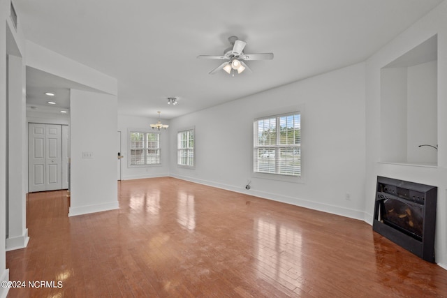 unfurnished living room with ceiling fan with notable chandelier and hardwood / wood-style floors