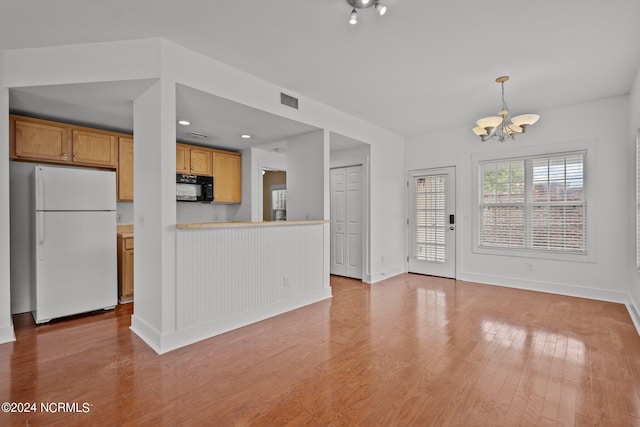 kitchen with hanging light fixtures, kitchen peninsula, white fridge, light hardwood / wood-style flooring, and a chandelier