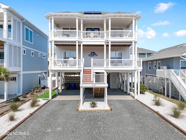 raised beach house with stairway, driveway, a balcony, and a carport