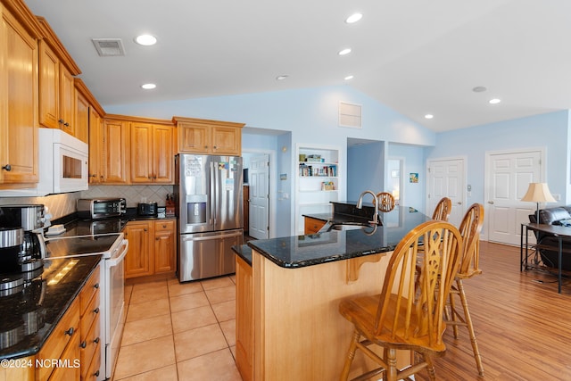 kitchen with a breakfast bar, vaulted ceiling, visible vents, a sink, and white appliances
