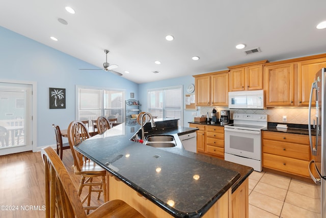 kitchen featuring an island with sink, white appliances, sink, light hardwood / wood-style floors, and vaulted ceiling