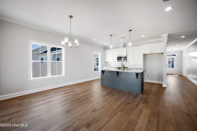 kitchen featuring a breakfast bar, decorative light fixtures, white cabinets, backsplash, and a large island with sink