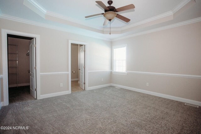 unfurnished bedroom with ornamental molding, a raised ceiling, a closet, and a walk in closet