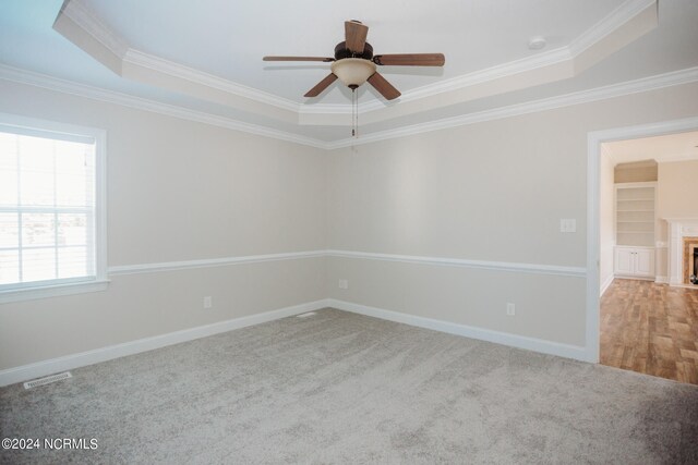 unfurnished room with ceiling fan, light colored carpet, a tray ceiling, and crown molding