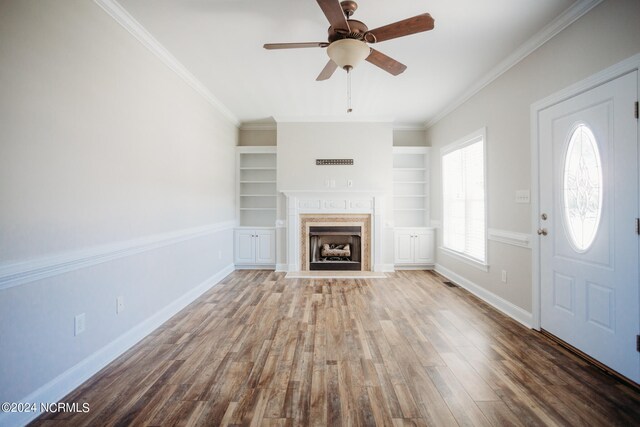 unfurnished living room featuring wood-type flooring, built in features, crown molding, and ceiling fan