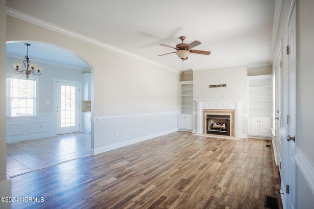 unfurnished living room featuring crown molding, built in shelves, and hardwood / wood-style flooring