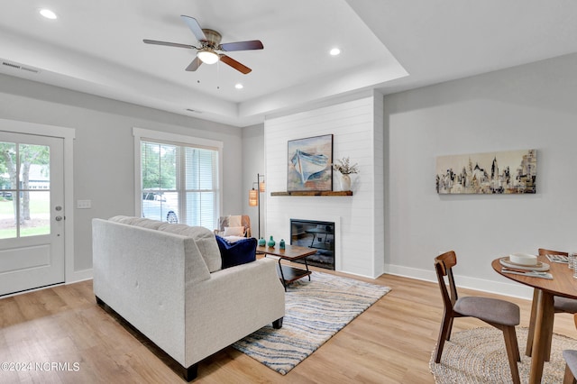 living room featuring hardwood / wood-style flooring, a fireplace, a raised ceiling, and ceiling fan