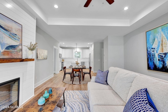 living room featuring ceiling fan, a large fireplace, and light wood-type flooring