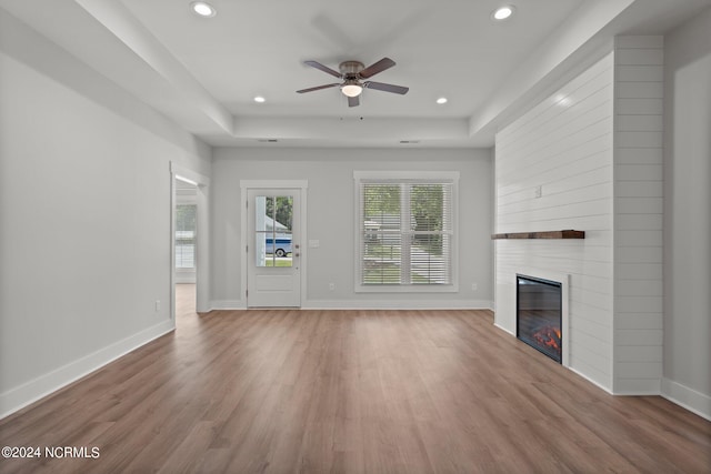 unfurnished living room featuring a tray ceiling, a fireplace, and wood-type flooring