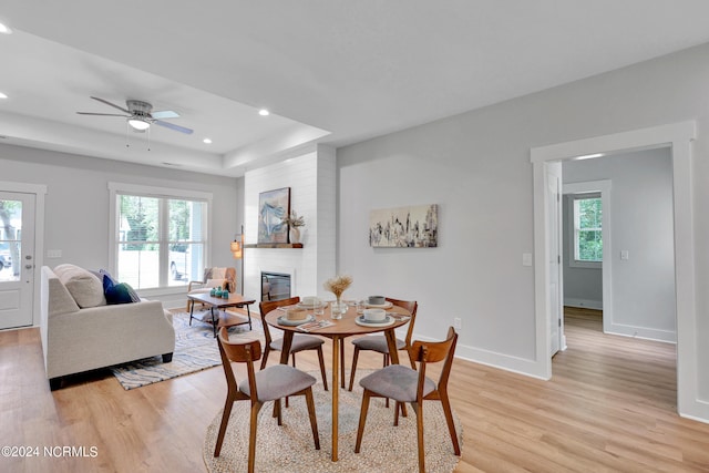 dining space featuring a healthy amount of sunlight, a fireplace, a tray ceiling, and light wood-type flooring