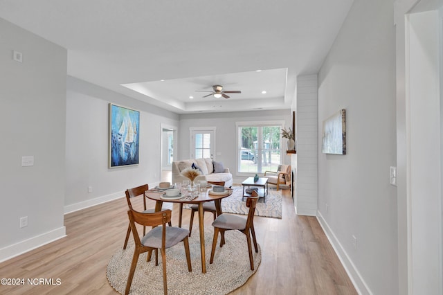 dining area with ceiling fan, a tray ceiling, and light hardwood / wood-style floors