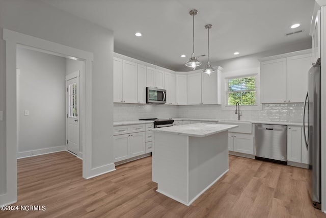 kitchen with a kitchen island, appliances with stainless steel finishes, white cabinetry, sink, and hanging light fixtures