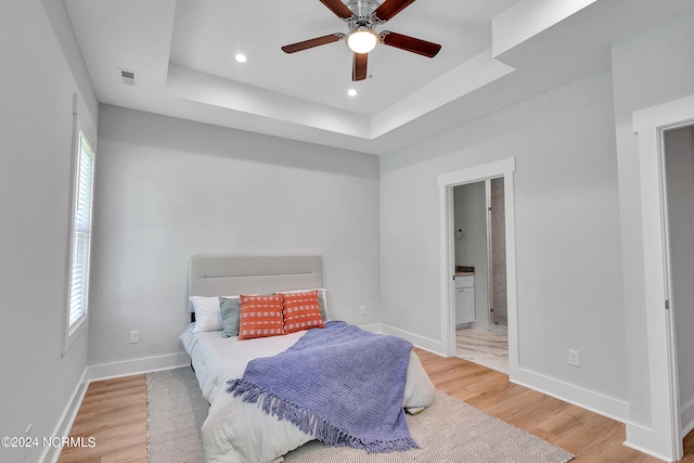 bedroom featuring a tray ceiling, hardwood / wood-style floors, ensuite bath, and ceiling fan