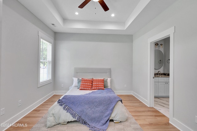 bedroom with hardwood / wood-style flooring, ensuite bath, a raised ceiling, and ceiling fan