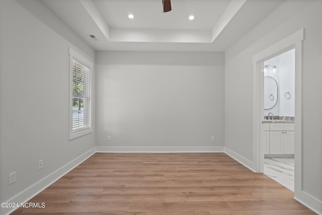 spare room featuring ceiling fan, sink, a raised ceiling, and light hardwood / wood-style floors