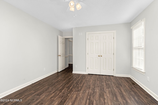 unfurnished bedroom with dark wood-type flooring, a closet, multiple windows, and ceiling fan