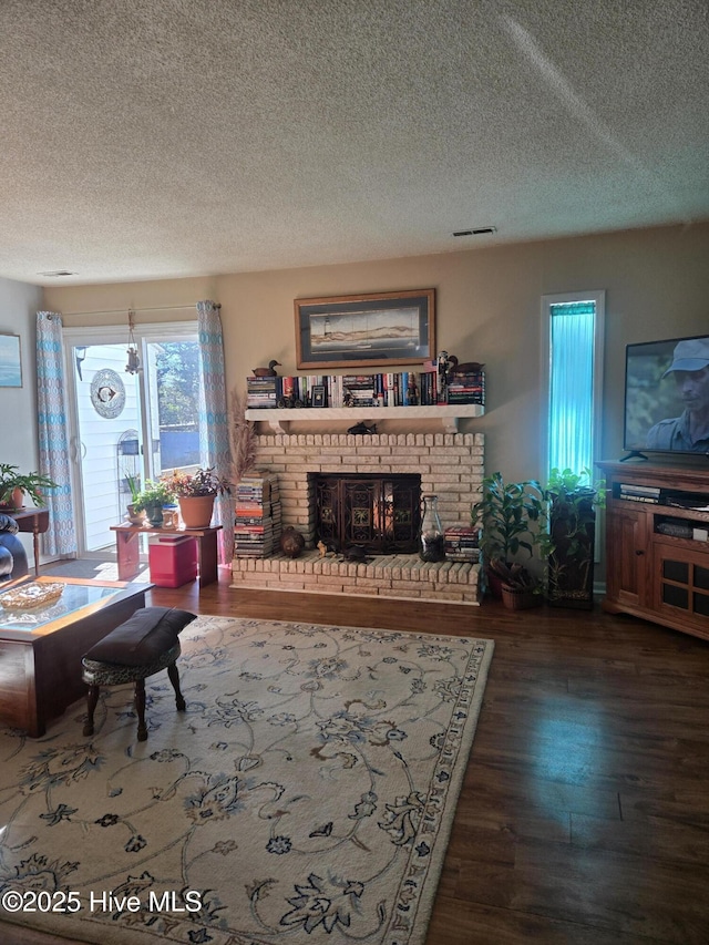 living room with a textured ceiling, a brick fireplace, and dark hardwood / wood-style floors