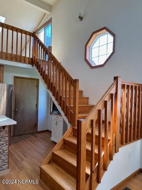 staircase featuring wood-type flooring and vaulted ceiling with beams