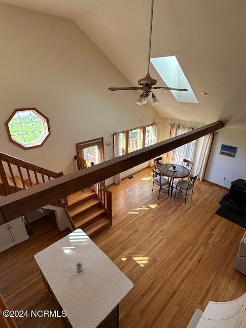 living room featuring high vaulted ceiling, ceiling fan, a skylight, and dark wood-type flooring