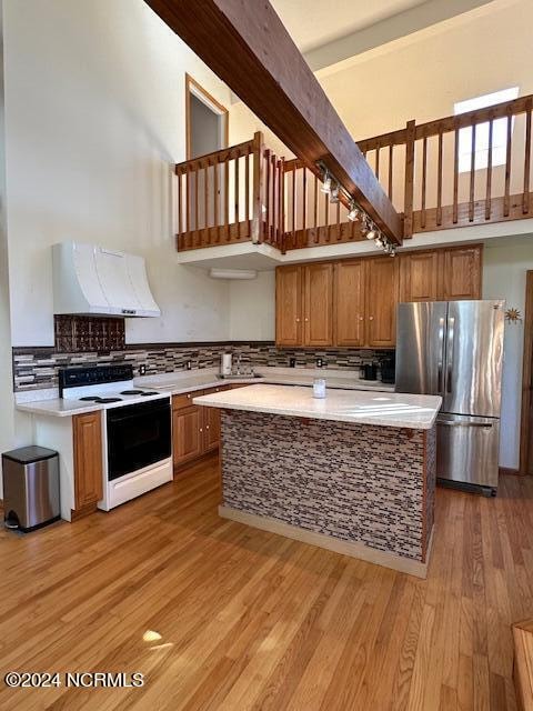 kitchen with premium range hood, light hardwood / wood-style floors, white range with electric stovetop, a high ceiling, and stainless steel fridge